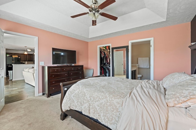 bedroom featuring a walk in closet, ensuite bath, black refrigerator with ice dispenser, a tray ceiling, and a closet