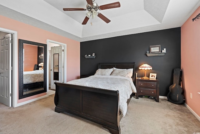 bedroom featuring a tray ceiling, ceiling fan, light carpet, and baseboards