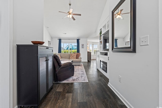 living area featuring a ceiling fan, baseboards, vaulted ceiling, and dark wood-style floors
