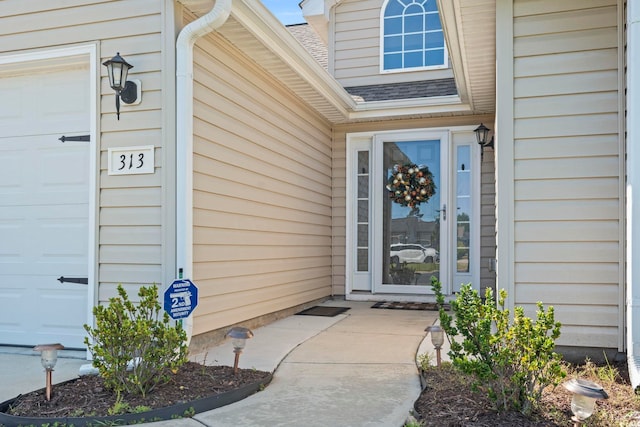 view of exterior entry featuring a garage and roof with shingles