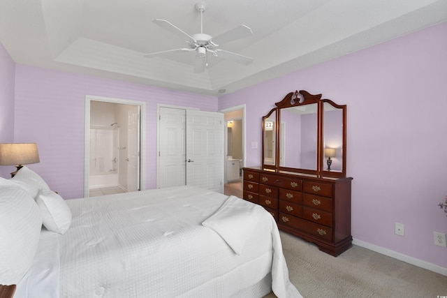 bedroom with connected bathroom, ceiling fan, light colored carpet, baseboards, and a tray ceiling