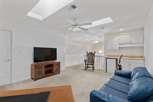 living room featuring vaulted ceiling with skylight, light carpet, a ceiling fan, and visible vents
