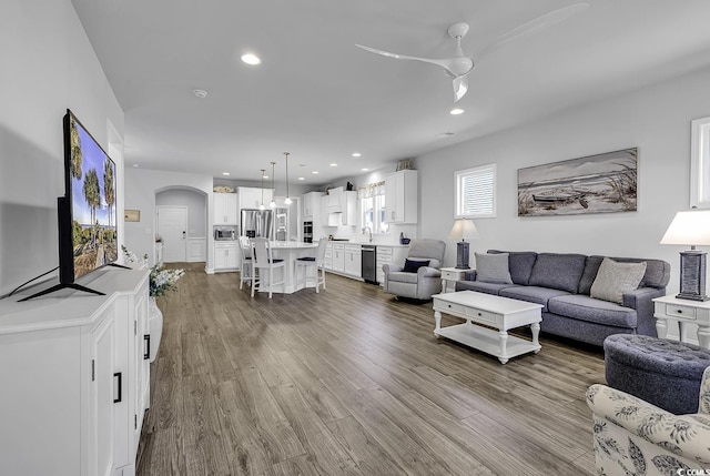 living area with arched walkways, ceiling fan, recessed lighting, and wood finished floors
