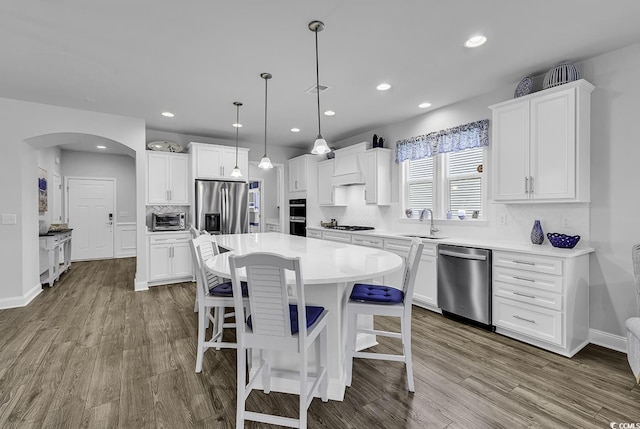 kitchen featuring a sink, dark wood-style floors, tasteful backsplash, arched walkways, and appliances with stainless steel finishes