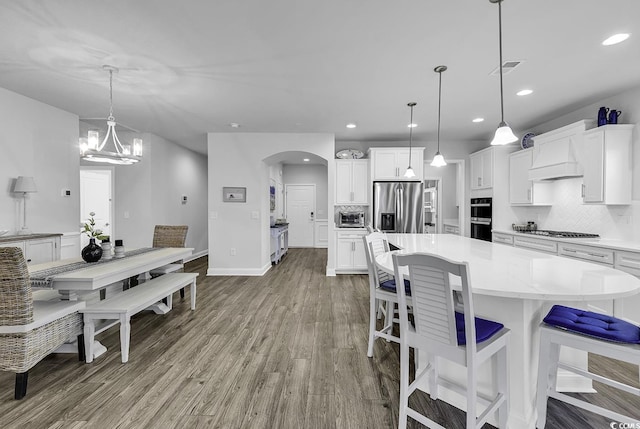 kitchen featuring arched walkways, appliances with stainless steel finishes, wood finished floors, and tasteful backsplash