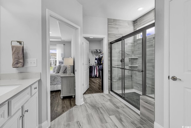 ensuite bathroom with vanity, baseboards, a walk in closet, and a shower stall