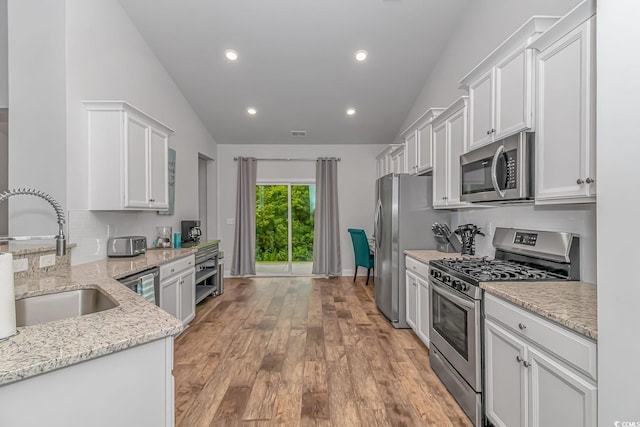 kitchen with white cabinets, appliances with stainless steel finishes, a sink, light wood-style flooring, and lofted ceiling