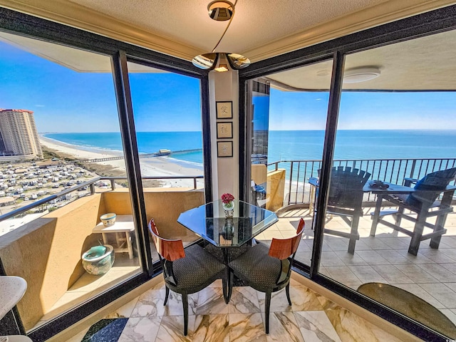 dining room with view of water and beach, light marble finish floors, and a textured ceiling