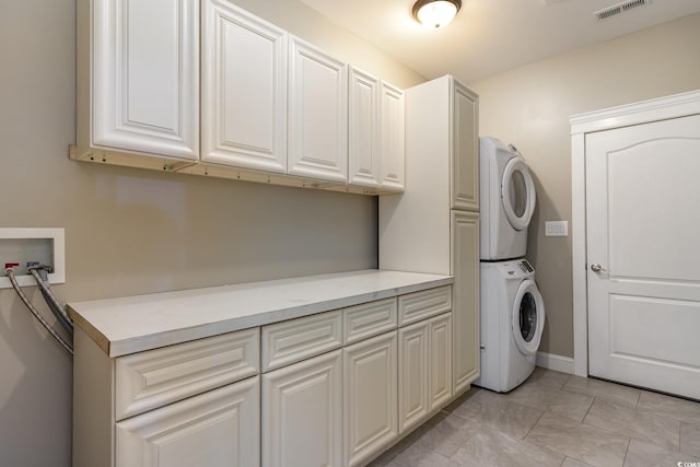 laundry area featuring cabinet space, baseboards, stacked washing maching and dryer, and visible vents