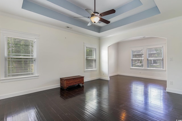 empty room featuring arched walkways, visible vents, a tray ceiling, and a wealth of natural light