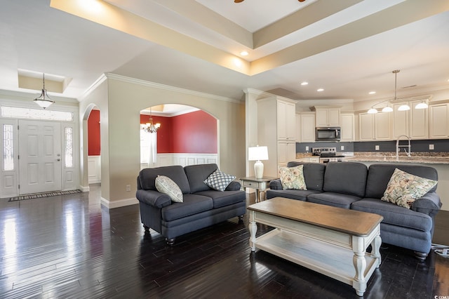 living room featuring crown molding, arched walkways, a wainscoted wall, dark wood-style floors, and an inviting chandelier
