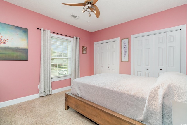 bedroom featuring visible vents, multiple closets, baseboards, ceiling fan, and light colored carpet