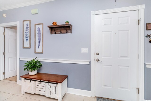 doorway with crown molding, light tile patterned flooring, and baseboards