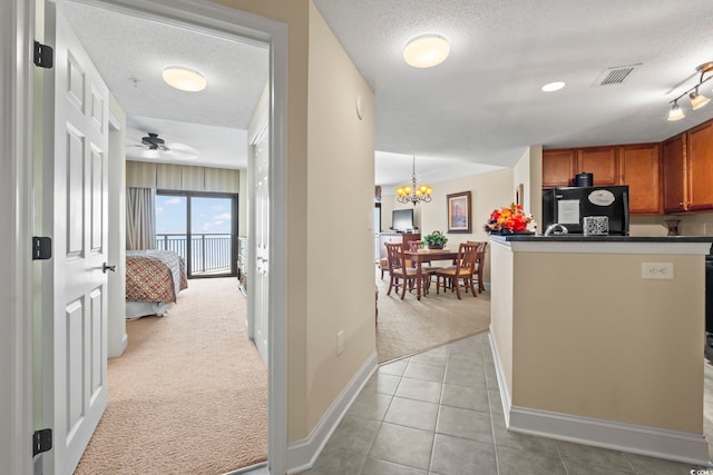 kitchen with fridge, brown cabinetry, light carpet, and a textured ceiling