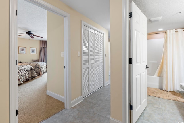 hallway with baseboards, a textured ceiling, light tile patterned floors, and light carpet