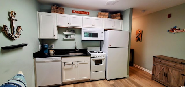kitchen with dark countertops, a sink, light wood-style floors, white appliances, and white cabinetry