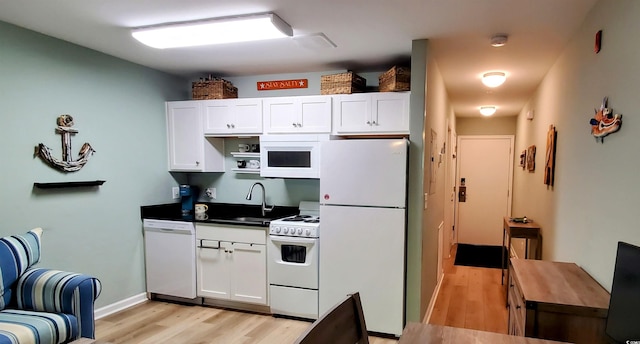 kitchen featuring white cabinets, dark countertops, a sink, white appliances, and light wood-style flooring