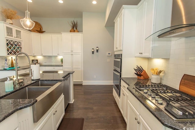 kitchen with decorative backsplash, wall chimney exhaust hood, white cabinetry, a sink, and appliances with stainless steel finishes
