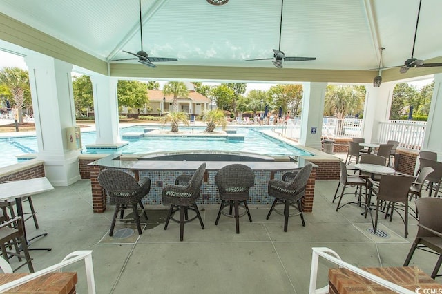 view of patio with an outdoor bar, a ceiling fan, a community pool, and fence