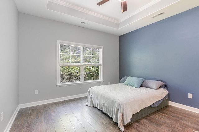 bedroom with wood finished floors, crown molding, a tray ceiling, and baseboards