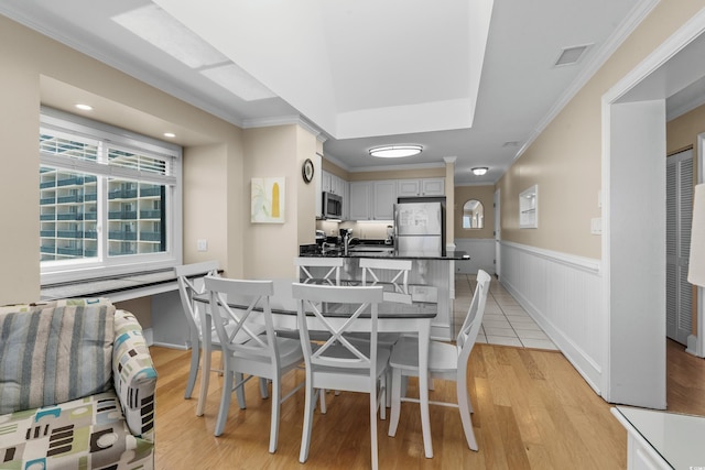 dining space with wainscoting, visible vents, ornamental molding, and light wood-style flooring
