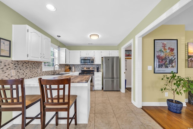 kitchen with a peninsula, a breakfast bar, a sink, white cabinets, and appliances with stainless steel finishes