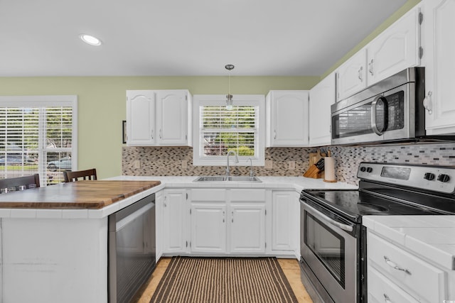 kitchen with a sink, stainless steel appliances, white cabinetry, and plenty of natural light