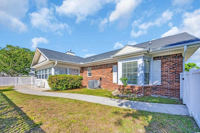 back of house featuring a yard, brick siding, central AC, and fence
