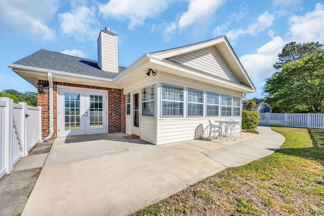 back of house with fence, brick siding, a chimney, a patio area, and french doors