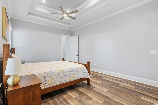 bedroom featuring crown molding, a tray ceiling, baseboards, and wood finished floors