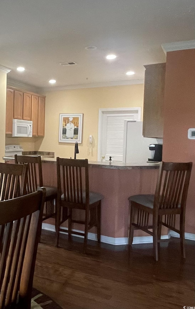 kitchen with recessed lighting, dark wood-style flooring, a kitchen bar, and white appliances