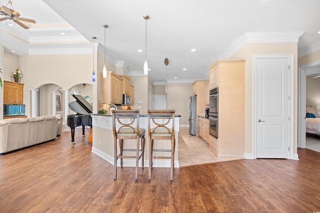 kitchen featuring open floor plan, a breakfast bar area, ceiling fan, cream cabinetry, and appliances with stainless steel finishes