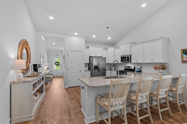 kitchen with a sink, appliances with stainless steel finishes, light stone countertops, and a peninsula