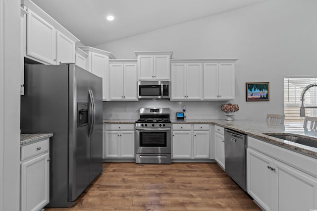 kitchen with lofted ceiling, white cabinets, a sink, appliances with stainless steel finishes, and backsplash