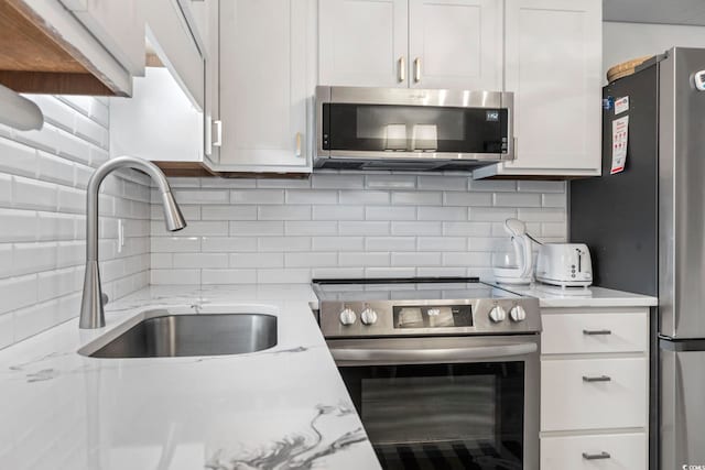 kitchen with a sink, appliances with stainless steel finishes, decorative backsplash, and white cabinetry
