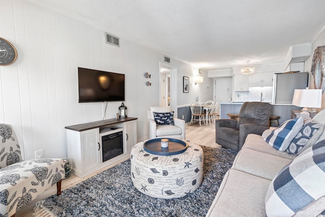 living room featuring visible vents, ornamental molding, and light wood finished floors