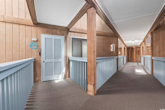 corridor featuring wood walls, carpet, and beam ceiling