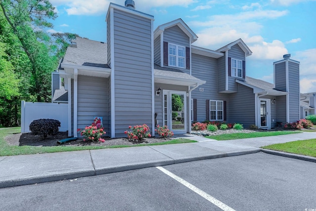 townhome / multi-family property with a shingled roof, uncovered parking, fence, and a chimney