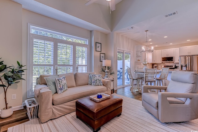 living area with visible vents, wood finished floors, baseboards, ceiling fan with notable chandelier, and recessed lighting