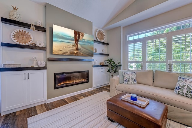 living area featuring a glass covered fireplace, a healthy amount of sunlight, wood finished floors, and lofted ceiling