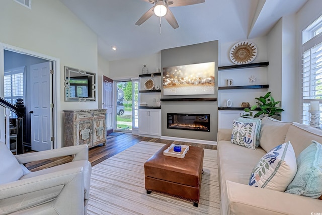 living room with ceiling fan, a glass covered fireplace, plenty of natural light, and wood finished floors