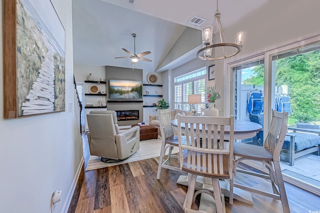 dining area featuring a glass covered fireplace, ceiling fan with notable chandelier, wood finished floors, lofted ceiling, and visible vents