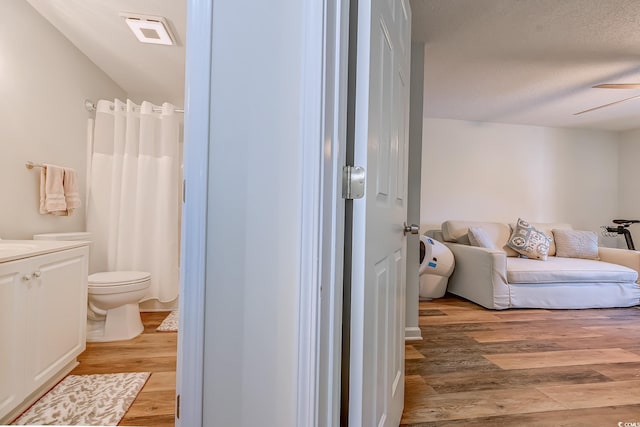 bathroom with ceiling fan, a textured ceiling, wood finished floors, curtained shower, and toilet