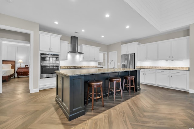 1136 Doubloon Dr, North Myrtle Beach, SC 29582 - kitchen with wall chimney range hood, a breakfast bar area, appliances with stainless steel finishes, white cabinets, and an island with sink