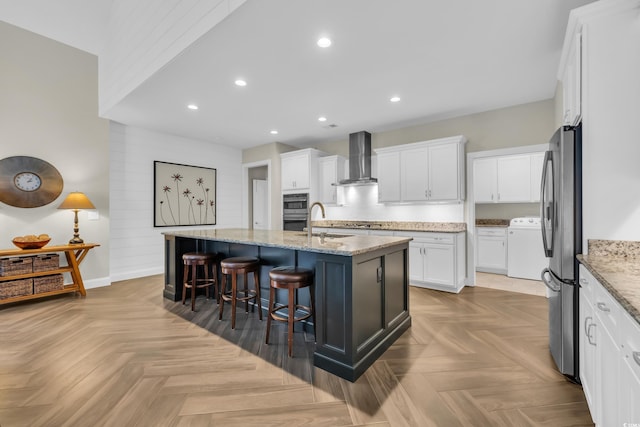 1136 Doubloon Dr, North Myrtle Beach, SC 29582 - kitchen with an island with sink, wall chimney range hood, white cabinetry, a sink, and appliances with stainless steel finishes