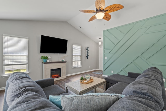 living room featuring a tiled fireplace, a ceiling fan, baseboards, wood finished floors, and lofted ceiling