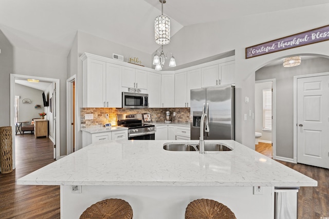 kitchen with white cabinetry, arched walkways, tasteful backsplash, a sink, and appliances with stainless steel finishes