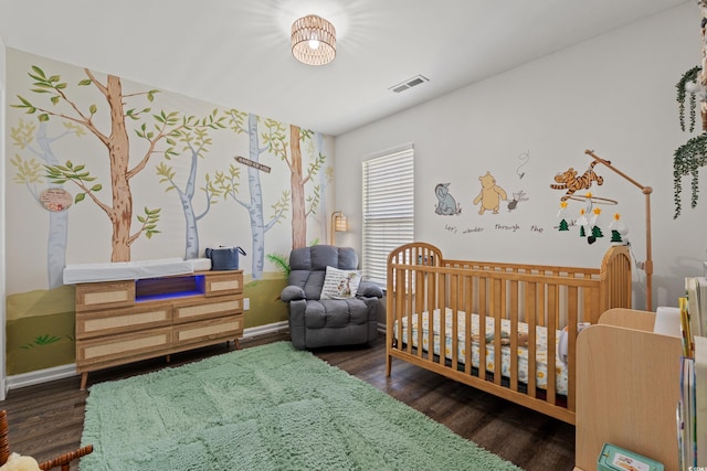 bedroom featuring baseboards, visible vents, a crib, and wood finished floors