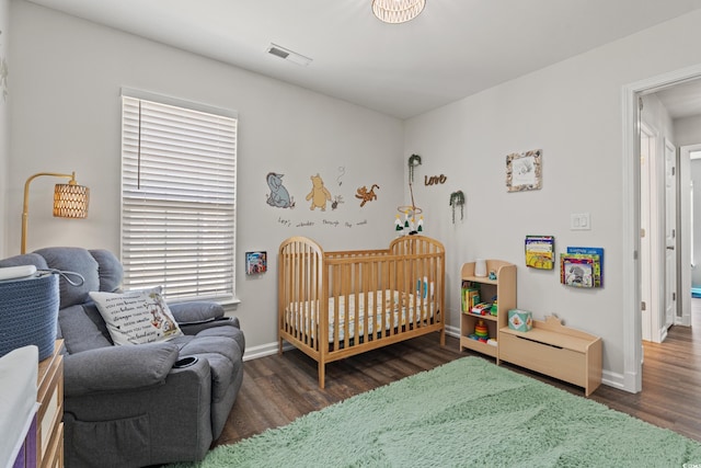 bedroom featuring visible vents, baseboards, wood finished floors, and a nursery area