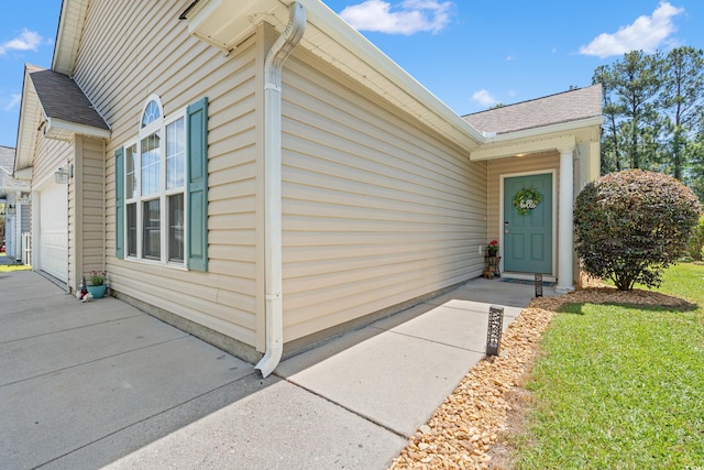 property entrance featuring a garage, a shingled roof, and concrete driveway